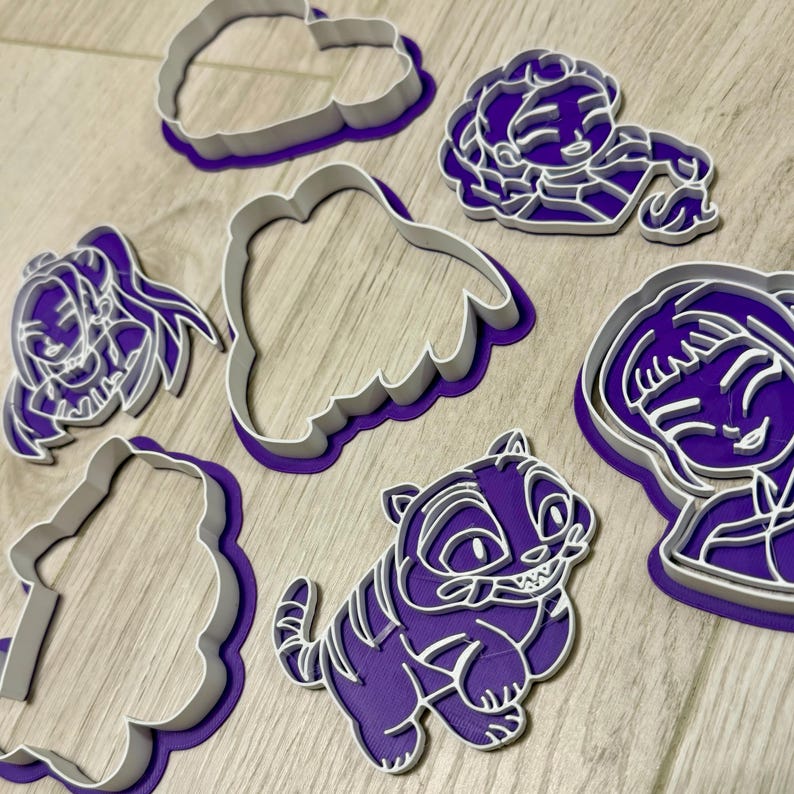 Pode incluir: Uma cole&ccedil;&atilde;o de cortadores de biscoitos roxos e brancos em v&aacute;rias formas, incluindo um tigre, uma nuvem e o rosto de uma menina. Os cortadores s&atilde;o feitos de pl&aacute;stico e s&atilde;o projetados para assar. A imagem &eacute; tirada de cima.