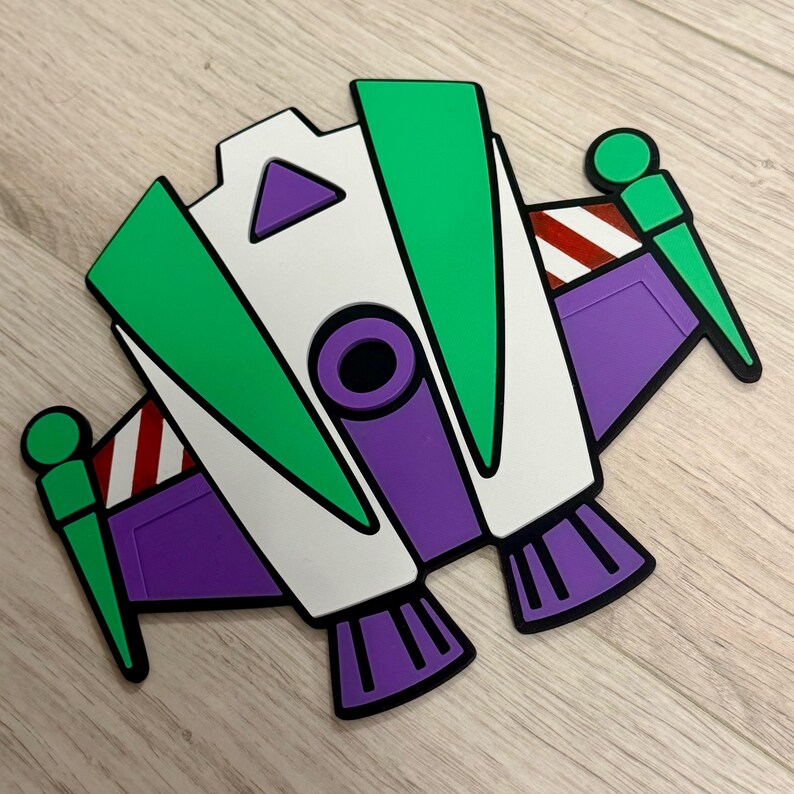May include: A colorful, stylized image of a spaceship toy in green, white, purple, and red. The toy has a black outline and is set against a light wood grain background. The design is reminiscent of a popular animated character.