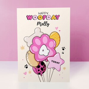 K&ouml;nnte beinhalten: Eine rosa und wei&szlig;e Geburtstagskarte mit dem Text "Happy Woofday Molly" und einer Cartoon-Illustration von ballons in Form von Pfoten mit einer Nummer 4 auf einem davon.