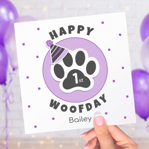 Puede incluir: Tarjeta de felicitaci&oacute;n cuadrada con las palabras "HAPPY WOOFDAY" y el nombre "Bailey". La tarjeta presenta una huella de pata con un gorro de fiesta y el n&uacute;mero "1st" dentro de un c&iacute;rculo lila, con lunares morados.