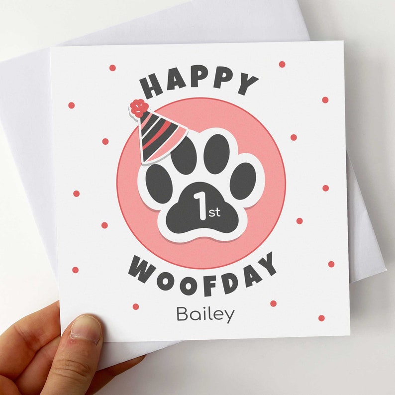 Puede incluir: Tarjeta de felicitaci&oacute;n cuadrada con fondo blanco y lunares rojos. Presenta un c&iacute;rculo rosa con una huella de pata negra y un gorro de fiesta. Las palabras "HAPPY WOOFDAY 1st" est&aacute;n impresas en la tarjeta, junto con el nombre "Bailey".