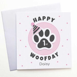 Puede incluir: Tarjeta de felicitaci&oacute;n cuadrada con sobre blanco. La tarjeta presenta un c&iacute;rculo rosa con una huella de pata negra y un gorro de fiesta. El texto dice "HAPPY WOOFDAY 1st Daisy" con lunares rosas.