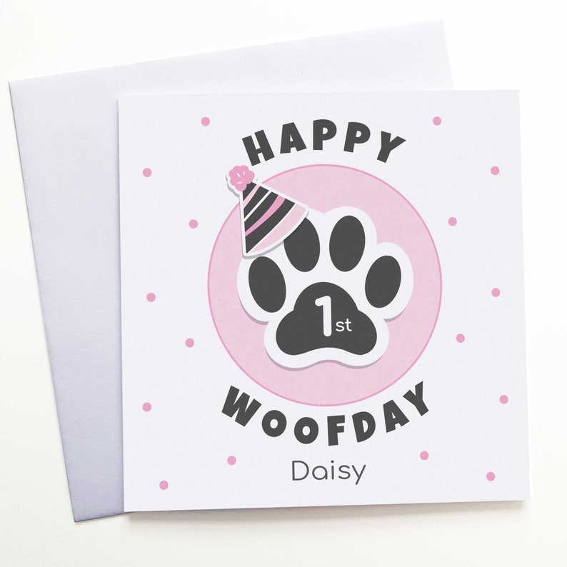 Puede incluir: Tarjeta de felicitaci&oacute;n cuadrada con sobre blanco. La tarjeta presenta un c&iacute;rculo rosa con una huella de pata negra y un gorro de fiesta. El texto dice "HAPPY WOOFDAY 1st Daisy" con lunares rosas.