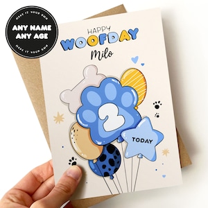 K&ouml;nnte beinhalten: Eine Geburtstagskarte mit einem Pfotenabdruck-Ballon mit der Nummer 2 darauf. Die Karte lautet "Happy Woofday Milo" und "Today".