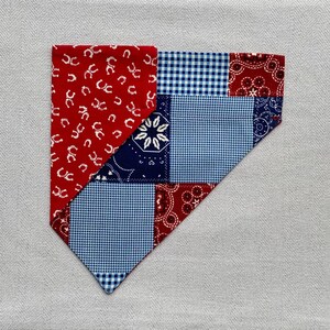 Peut inclure: Un bandana patchwork avec des motifs variés. Il présente du tissu rouge avec des fers à cheval blancs, du vichy bleu, un imprimé cachemire bleu marine et du tissu cachemire rouge. Le bandana a un bord inférieur pointu.