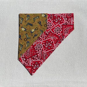 May include: A two-tone bandana. One side is brown with cowboy boots, hats, and stars. The other side is red with a white paisley pattern. The bandana is folded diagonally. The measurements are in centimetres.