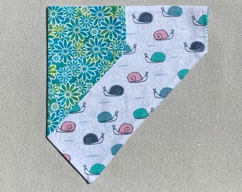 May include: A triangular pet bandana with two distinct fabric patterns. One side features a teal and white floral design, while the other displays a pattern of snails in pink, teal, and navy blue on a white background. The bandana is likely for a dog or cat.