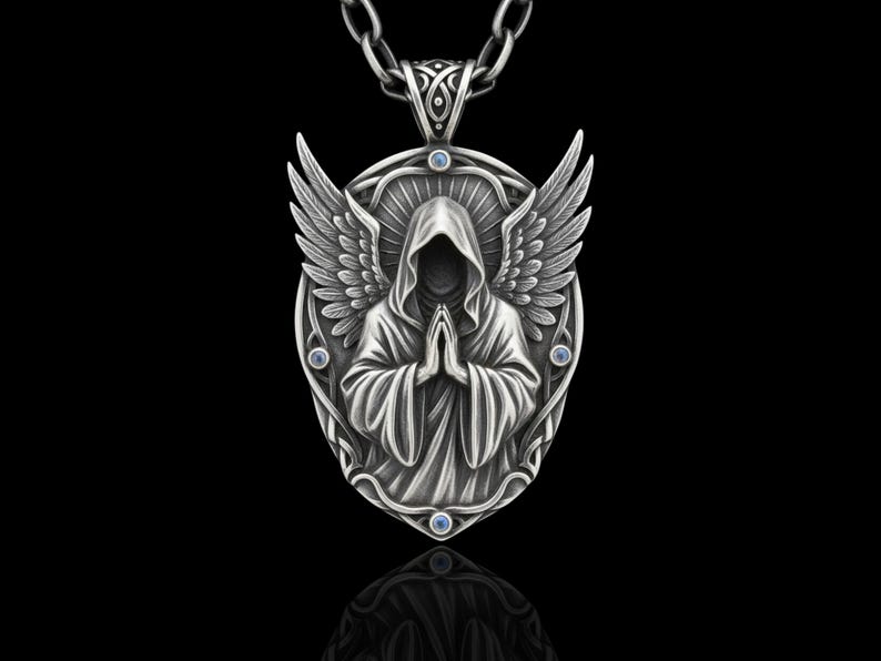 Puede incluir: Un collar con colgante de plata que representa una figura encapuchada con las manos juntas, alas de &aacute;ngel y detalles azules. El colgante ovalado cuelga de una cadena de plata. El dise&ntilde;o tiene detalles intrincados y un tema g&oacute;tico.