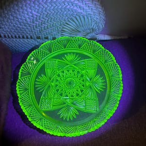 May include: A bright green glass plate with a geometric design. The plate has a scalloped edge and is made of uranium glass, which glows under a black light.