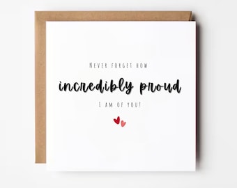 May include: A white greeting card with the message "Never forget how incredibly proud I am of you!" in black script. Two small red hearts are at the bottom. The card is in a brown envelope.