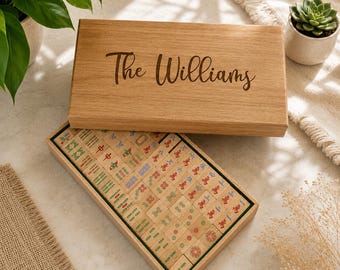 May include: A rectangular wooden box with a sliding lid engraved with the text The Williams, containing a set of light-colored mahjong tiles featuring various red, green, and blue symbols, characters, and patterns arranged in neat rows.