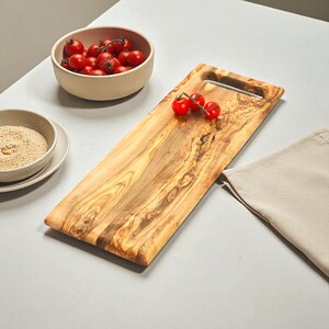 May include: A rectangular wooden chopping board with a handle, showing a natural wood grain. Small red tomatoes are placed on the board. A small bowl of tomatoes and a bowl of spices are also present.