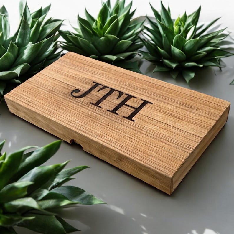 K&ouml;nnte beinhalten: Eine rechteckige Holzschachtel mit hellbrauner Maserung, auf deren Oberseite die Buchstaben JTH in einer dunklen Serifenschrift eingraviert sind. Die Schachtel hat einen glatten, flachen Deckel und eine kleine Aussparung an der Vorderkante zum &Ouml;ffnen.