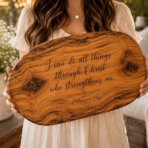 May include: An oval wooden serving board with a natural grain pattern and dark knots. The board is engraved with the text "I can do all things through Christ who strengthens me." followed by a small heart icon and "Philippians 4:13".