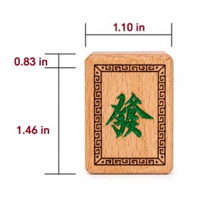 K&ouml;nnte beinhalten: Ein rechteckiger Mahjong-Spielstein aus Holz mit einem gr&uuml;nen, eingravierten chinesischen Schriftzeichen in der Mitte, umgeben von einem schwarzen geometrischen Rand. Der Stein ist 2,8 cm breit, 3,7 cm hoch und 2,1 cm dick.
