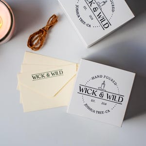 Custom logo rubber stamp on white product box lid and branded envelopes showing consistent candle business branding across multiple packaging surfaces