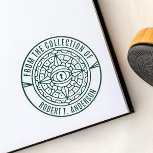 May include: A green ink stamp on white paper, featuring the text "FROM THE COLLECTION OF ROBERT T. ANDERSON" around a central eye and keyhole design. The stamp is partially visible, with a black border and a yellow shoe in the background.