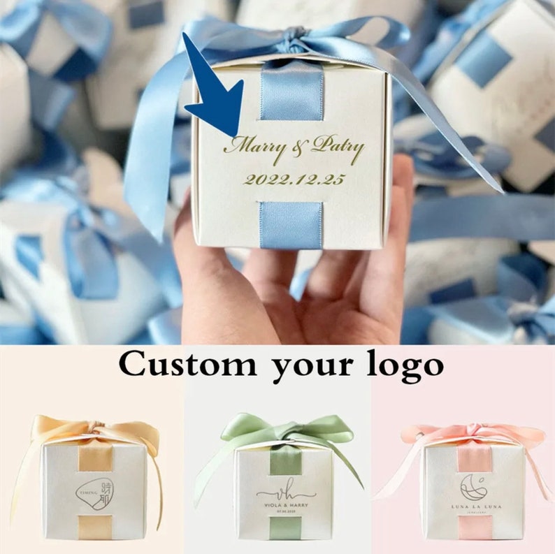 May include: A white gift box with a light blue ribbon and accents. The box is personalized with the text "Marry & Patry" and the date "2022.12.25". Additional boxes with different ribbon colors are shown.