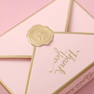 May include: A pink envelope with a gold seal and the words "Truly Yours" written in gold script. The envelope is decorated with a gold border and has the word "Specially" written on the bottom.