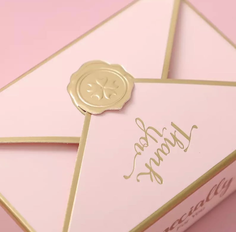 May include: A pink envelope with a gold seal and the words "Truly Yours" written in gold script. The envelope is decorated with a gold border and has the word "Specially" written on the bottom.