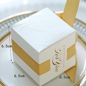 May include: A white square gift box with embossed floral patterns, measuring 6.5 cm on each side, wrapped with a gold ribbon. The box has the words "Especially For You" in gold script.