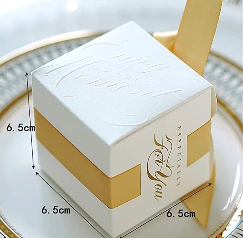 May include: A white square gift box with embossed floral patterns, measuring 6.5 cm on each side, wrapped with a gold ribbon. The box has the words "Especially For You" in gold script.