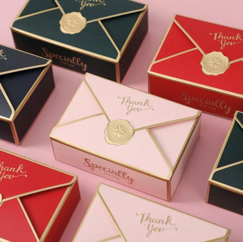 May include: Assortment of small, decorative boxes in pink, red, and black with gold accents. The boxes are shaped like envelopes and have the text "Thank You" and "Specially for you" printed on them.