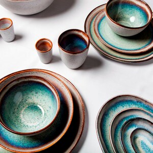 Op de afbeelding: Een set keramiek serviesgoed in tinten blauw, groen en bruin. De set bevat borden, kommen en bekers.