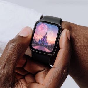 May include: A black smartwatch with a square face displaying a photo of Cinderella's castle at Walt Disney World with fireworks in the sky.