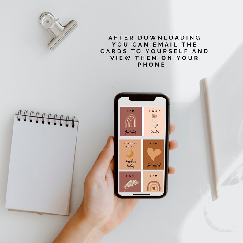 May include: A smartphone displaying affirmation cards with illustrations and text. The cards include phrases like "I am Grateful", "I am a Leader", "I Choose to be Positive Today", and "I am Successful".