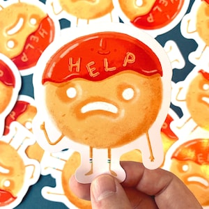 May include: A sticker of a cartoon doughnut with a red icing topping that says "HELP" in white letters. The doughnut has a distressed expression with white eyes and a frown. The doughnut has arms and legs and is standing on a white background.