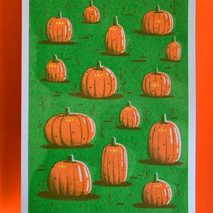 May include: A green background with 13 orange pumpkins with happy faces. The pumpkins are of different sizes and are scattered across the background.