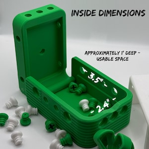 May include: A bright green, hinged storage box with the words "INSIDE DIMENSIONS" printed on the top. The box is open, revealing a 8.9 cm x 6.1 cm interior, approximately 2.5 cm deep. Several green and white screws are scattered around the box.