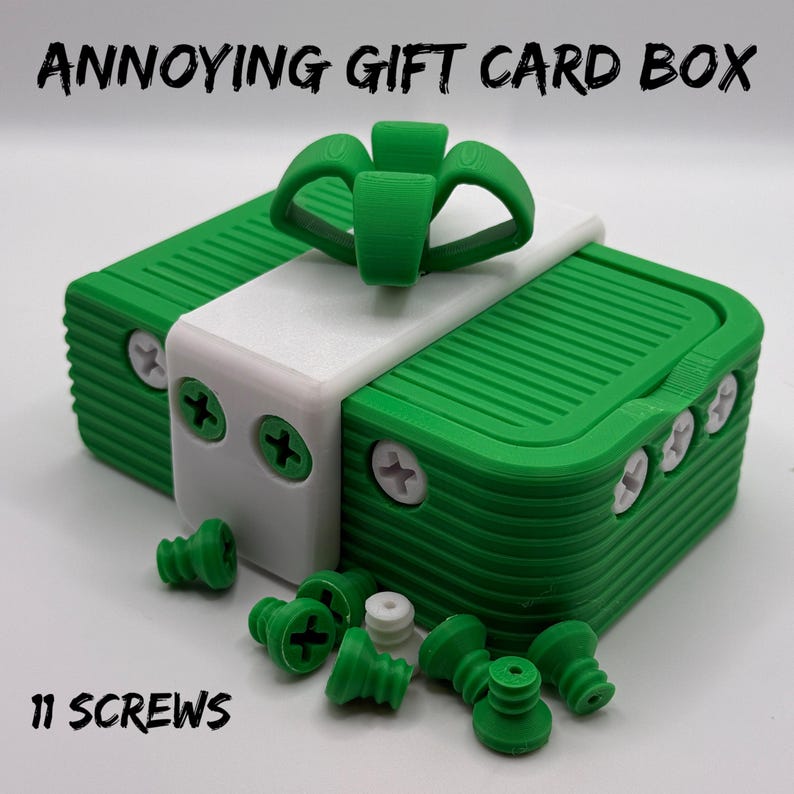 May include: A green and white gift card box with the text "ANNOYING GIFT CARD BOX" and "11 SCREWS". The box has a green bow on top and is surrounded by green screws.