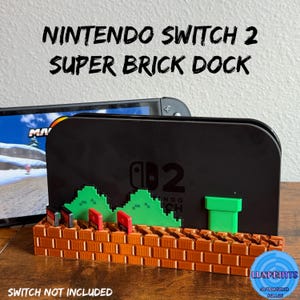 Peut inclure: Station d'accueil Nintendo Switch 2 Super Brick noire avec un design de briques et de collines vertes en pixels. La station d'accueil comporte des emplacements pour les cartouches de jeu et un tuyau vert. Le texte "NINTENDO SWITCH 2 SUPER BRICK DOCK" est affiché.