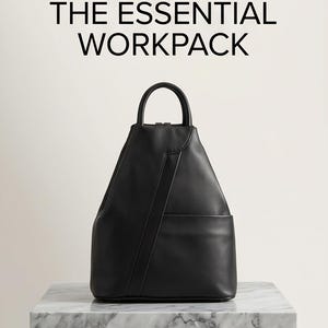 Puede incluir: Mochila negra con asa superior y bolsillo frontal, sobre fondo blanco. El texto "THE ESSENTIAL WORKPACK" se muestra encima de la mochila. La bolsa está colocada sobre una superficie de mármol.