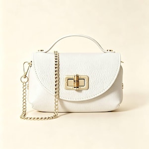 May include: A white textured leather handbag featuring a top handle and a detachable gold-tone chain shoulder strap. The front flap is secured with a rectangular gold-tone metal turn-lock closure that includes a small bamboo-style accent piece.