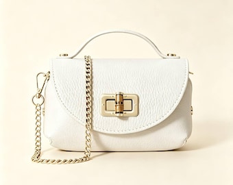 Puede incluir: Un bolso de mano de cuero blanco texturizado con un asa superior y una correa de hombro de cadena dorada desmontable. La solapa frontal se asegura con un cierre giratorio de metal dorado rectangular que incluye un pequeño detalle de bambú.