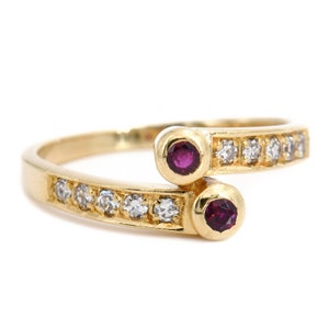 Könnte beinhalten: Ein goldener Ring mit zwei Rubinen und einer Reihe von Diamanten. Der Ring ist so konzipiert, dass er sich um den Finger legt.