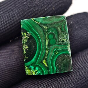Puede incluir: Una piedra rectangular de malaquita con una superficie pulida. La piedra presenta un color verde vibrante con patrones y texturas arremolinadas. Los patrones incluyen círculos concéntricos y formas irregulares.