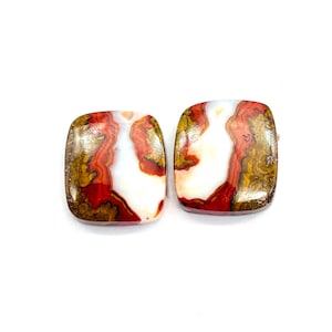 Puede incluir: Dos piedras preciosas cuadradas con esquinas redondeadas. Las piedras presentan una mezcla de colores, incluyendo blanco, rojo, marrón y dorado. Las piedras preciosas tienen un acabado pulido y brillante sobre un fondo blanco.