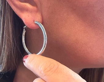 May include: A polished silver-tone hoop earring with a circular design and a hinged closure mechanism. The earring features a smooth, reflective metallic surface and a simple, continuous round shape that hangs from the earlobe.