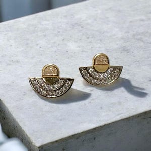 May include: A pair of gold earrings with a semi-circle design and a small round stone in the centre. The earrings are set with small clear stones.