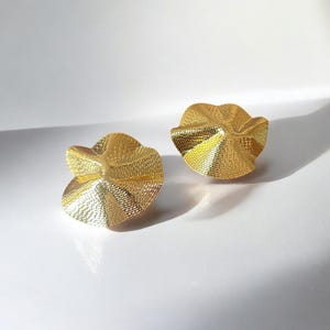 Könnte beinhalten: Ein Paar goldfarbene Ohrringe mit einem strukturierten, wellenförmigen und leicht asymmetrischen Design.