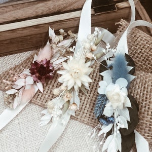 May include: Three dried flower wrist corsages with white satin ribbon. The corsages feature different colors and styles of dried flowers, including white, pink, blue, and burgundy.
