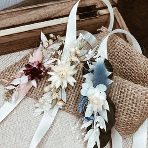 May include: Three dried flower wrist corsages with white satin ribbon. The corsages feature dried flowers in shades of white, cream, pink, burgundy, and blue.