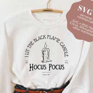 May include: White sweatshirt with a black graphic design that says "I Lit The Black Flame Candle 1993 Hocus Pocus Salem, MA".