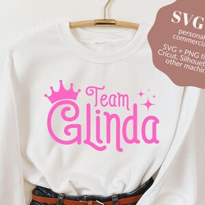 Pu&ograve; includere: Felpa bianca con una corona rosa, le parole "Team Glinda" e stelle scintillanti.