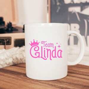 Pu&ograve; includere: Tazza in ceramica bianca con una corona rosa e il testo "Team Glinda" stampato su di essa.