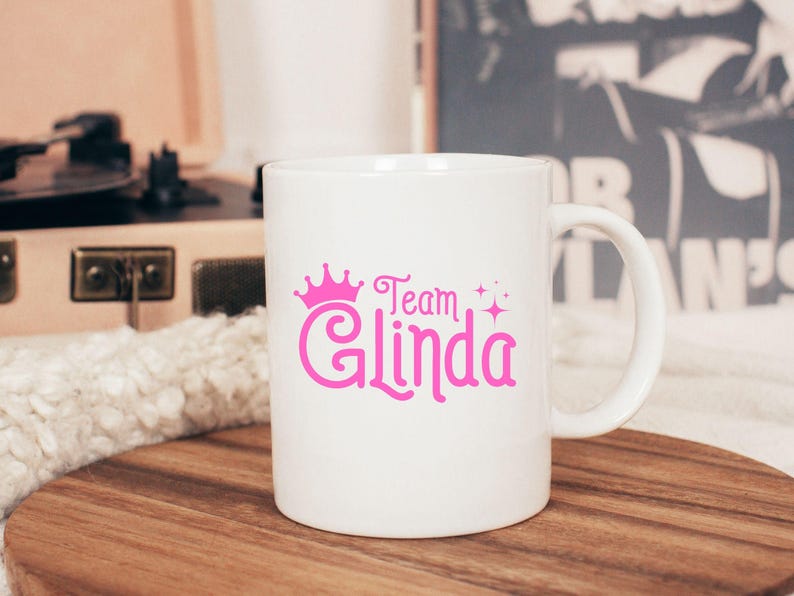 Pu&ograve; includere: Tazza in ceramica bianca con una corona rosa e il testo "Team Glinda" stampato su di essa.